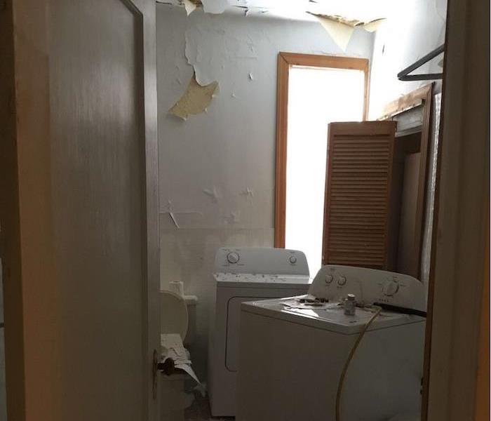 Room with damaged ceiling and debris on washer and dryer