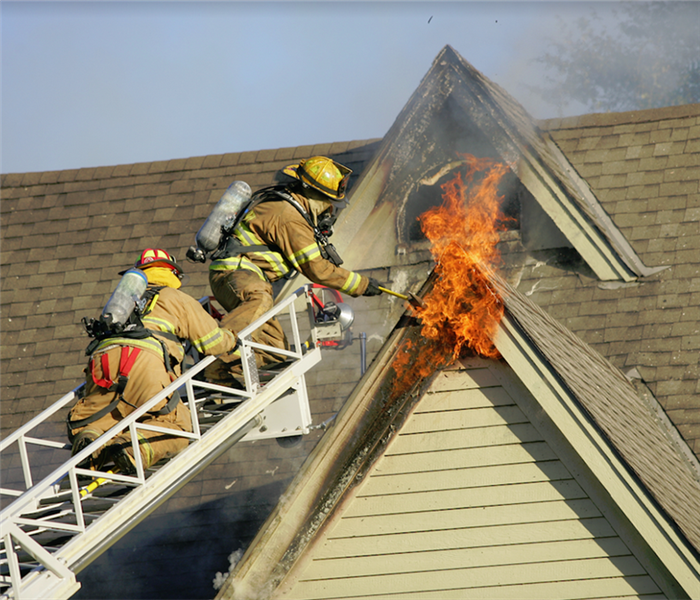 firemen standing on a ladder as they try to extinguish flames on the outside of a house