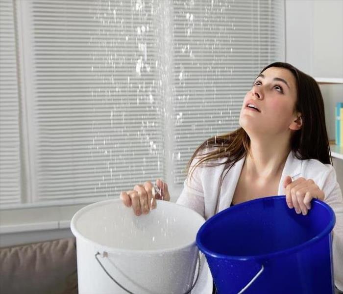 a woman holding buckets to catch water falling from her ceiling